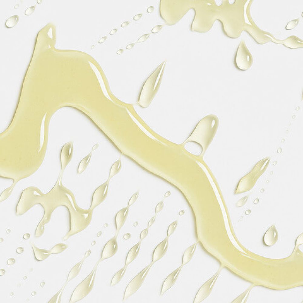 Texture oleosa della vitamina E contenuta nel balsamo labbra Vilo Lip Oil, con gocce e striature su sfondo bianco che evocano idratazione e nutrimento
