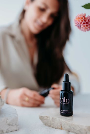 Foto di un boccetto di olio viso beauty caress di vilo cosmetics con la dottoressa Vittoria Lonetti sullo sfondo