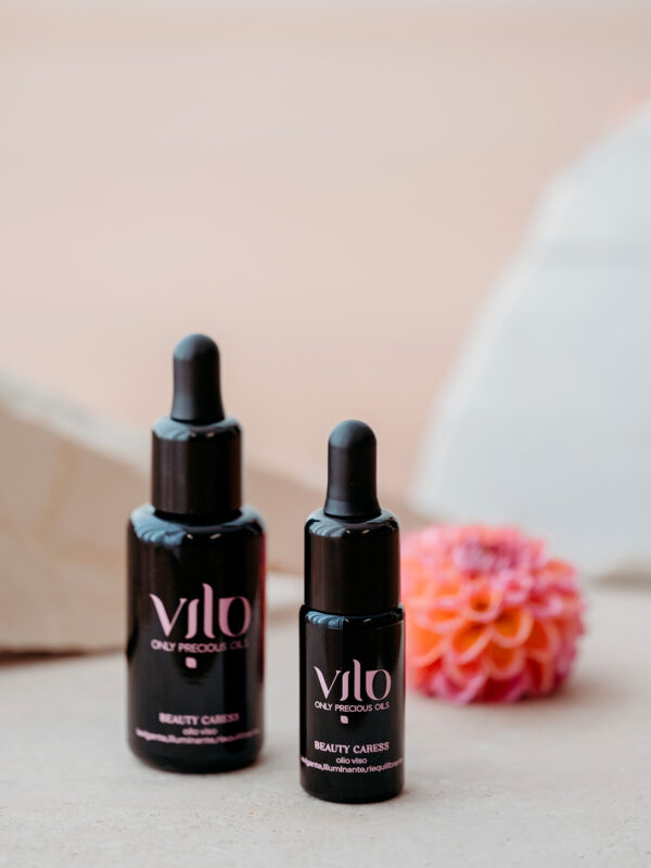 Foto di due boccetti di olio viso beauty caress di vilo cosmetics su sfondo di marmo e fiori